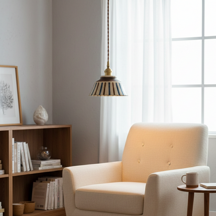 Suspension céramique rayée éclairant un fauteuil beige dans un coin lecture cosy