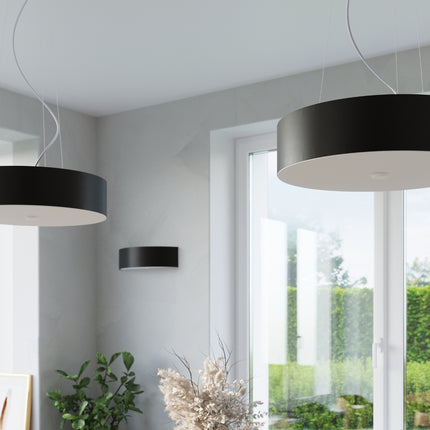 Détail de la suspension en tissu noir avec son diffuseur en verre blanc, près d'une fenêtre
