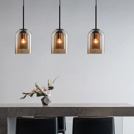 Trois suspensions cloche en double verre marron alignées au-dessus d'une table claire