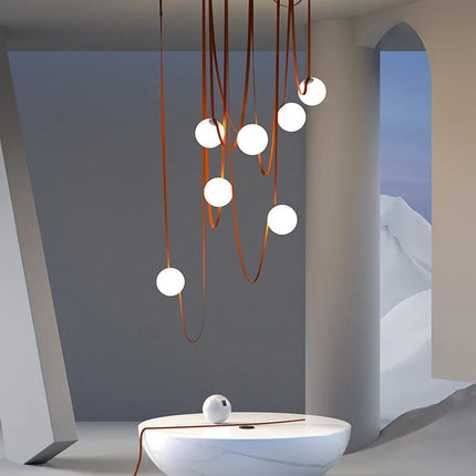 Détail du design de la suspension en cuir cognac, lanières souples et globes opalins, pour un intérieur raffiné.