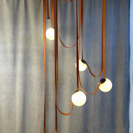 Suspension en cuir cognac déclinée en plusieurs globes pour une ambiance chaleureuse dans un grand espace.