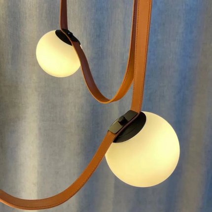 Suspension en cuir cognac et verre opalin apportant un éclairage doux au-dessus d'une salle à manger.