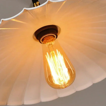 Détail de l'abat-jour festonné blanc et de son ampoule à filament ambré vue de dessous