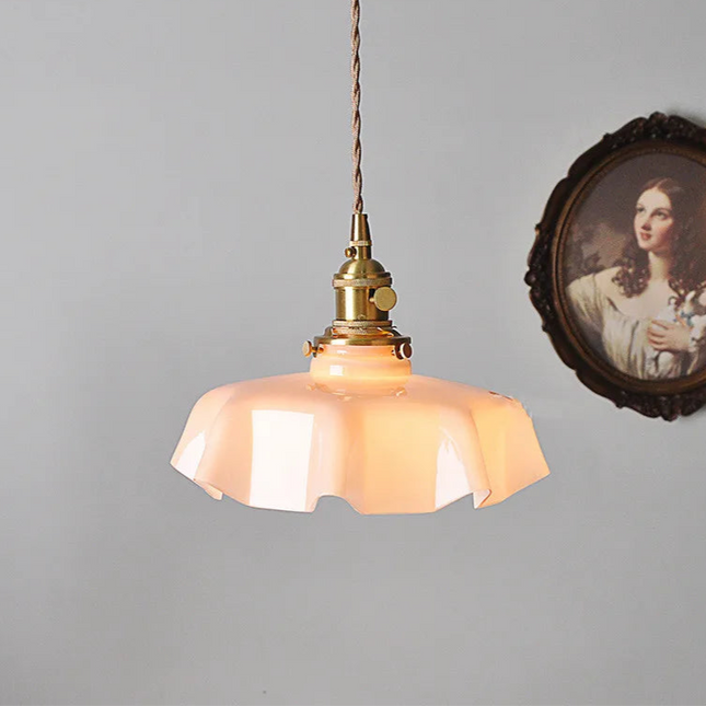 Suspension fleur en verre opalin rose allumée, lumière douce et cordon textile tressé au dessus d'un mur clair