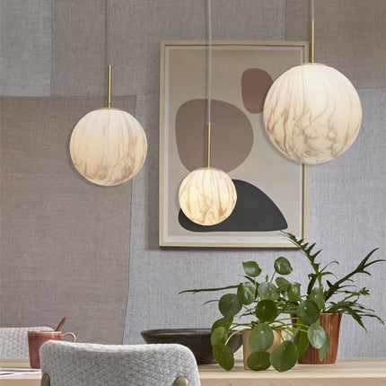 Suspensions globe effet marbre en plusieurs tailles suspendues devant un tableau abstrait