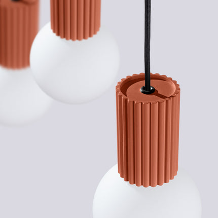 Suspension Halo 3 globes sur barre rouge ocre sur fond coloré, vue de trois quarts