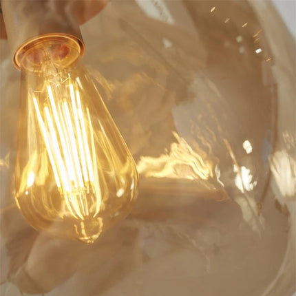 Zoom sur l'ampoule à filament visible à travers le verre ambre soufflé de la suspension Helsinki