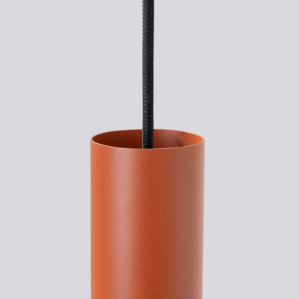 Suspension Long Cylindre 2 Rouge Ocre en Acier, vue sur fond coloré