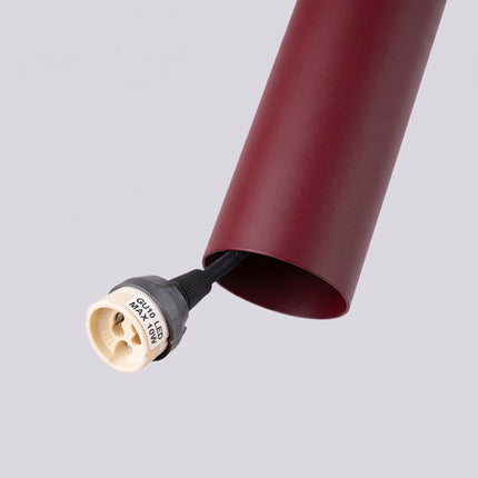Suspension Long Cylindre bordeaux sur fond coloré, vue de trois quarts