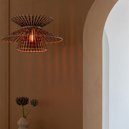 Suspension bambou tressé forme sablier allumée devant un mur terracotta, jeu d'ombres projetées