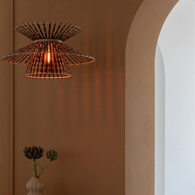 Suspension bambou tressé forme sablier allumée devant un mur terracotta, jeu d'ombres projetées