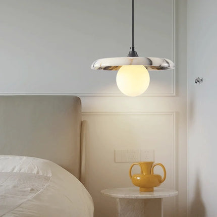 Suspension en marbre au-dessus d'un chevet dans une chambre beige, lumière chaude du globe opalin