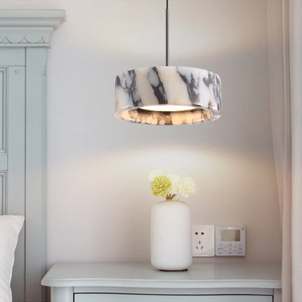 Suspension en marbre naturel diffusant une lumière douce au-dessus d'une table de chevet blanche