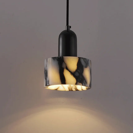 Suspension cylindrique en marbre veiné avec chapeau chrome noir, allumée sur fond gris