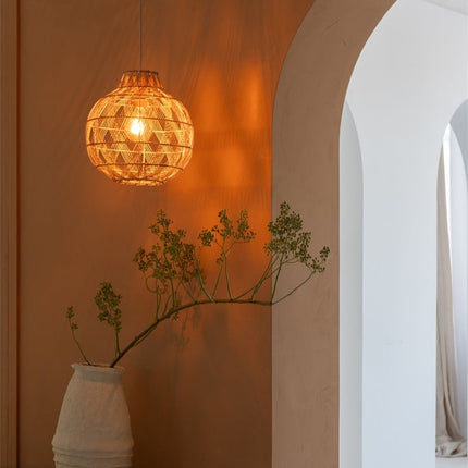 Suspension boule en bambou naturel allumée, lumière chaude projetée sur un mur terracotta