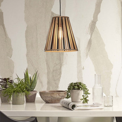 Suspension Merapi en bambou allumée au-dessus d'une table blanche entourée de plantes, lumière douce et enveloppante.