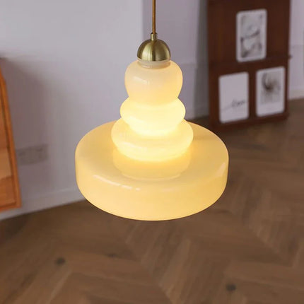 Suspension en verre soufflé crème diffusant une lumière douce au-dessus d'un parquet chevrons
