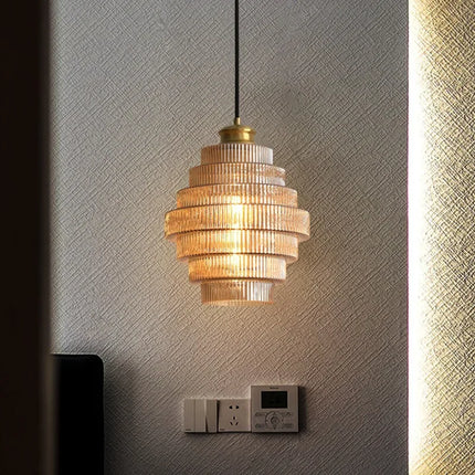 Suspension nordique en verre strié doré diffusant une lumière ambrée sur un mur texturé