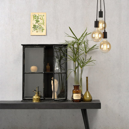 Suspension Oslo noire allumée près d'un meuble vitrine et de plantes dans une ambiance cocooning