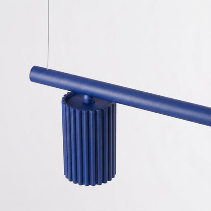 Suspension Oslo poutre 4 cylindres 122 cm bleu outremer sur fond coloré, vue de trois quarts