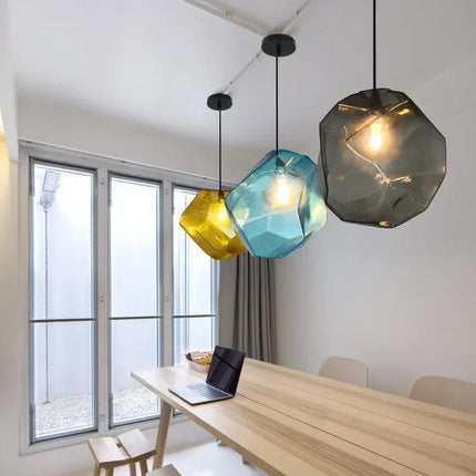 Trois suspensions pierre en verre jaune, bleu et gris fumé au-dessus d'une table à manger