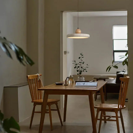 Suspension plate en travertin diffusant une lumière tamisée au-dessus d'une salle à manger