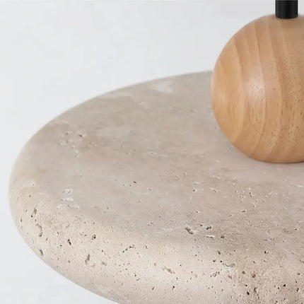 Gros plan sur la texture alvéolée du galet de travertin et la sphère en bois clair de la suspension