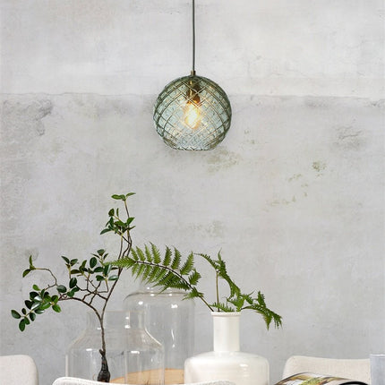 Suspension Venice globe en verre soufflé vert quadrillé suspendue devant un mur en béton brut