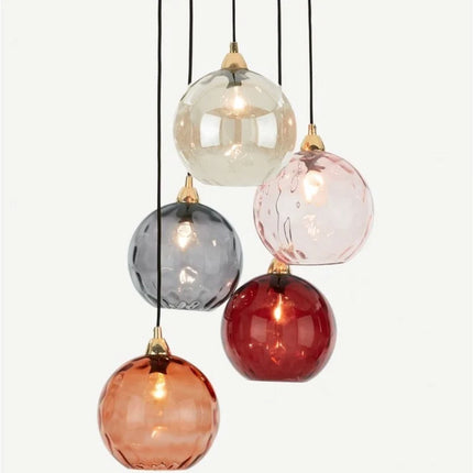 Grappe de cinq suspensions à globes en verre martelé multicolores sur fond clair, ampoules allumées