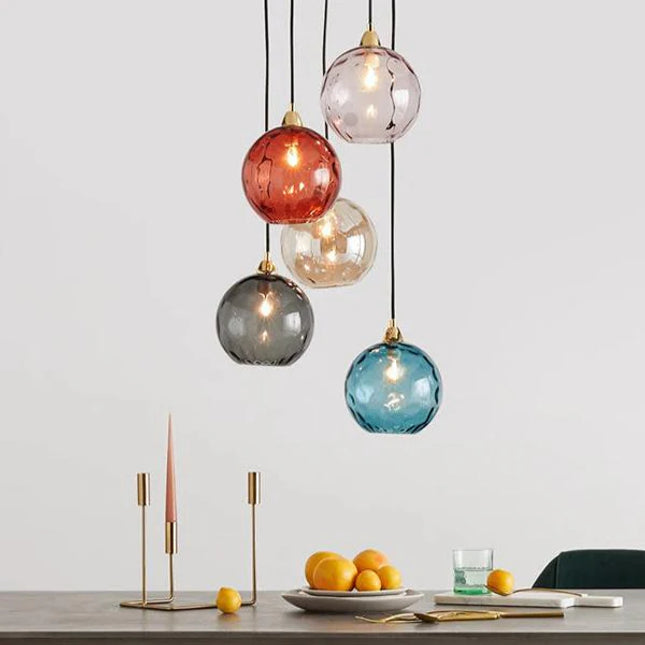 Grappe de cinq suspensions à globes en verre martelé coloré au-dessus d'une table, ampoules allumées