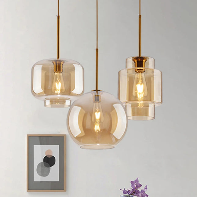 Trio de suspensions en verre ambré et laiton, formes jarre, globe et cylindre, ampoules à filament allumées