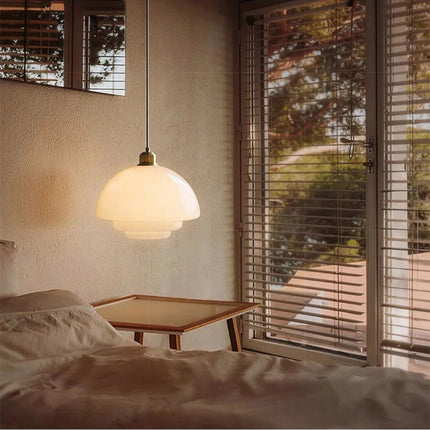 Suspension dôme en verre opalin crème allumée près d'un lit dans une chambre