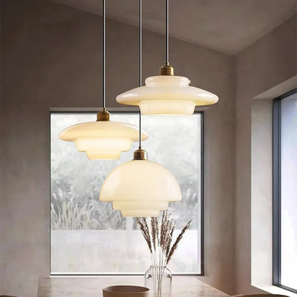 Les trois modèles de suspension en verre opalin crème devant une fenêtre lumineuse