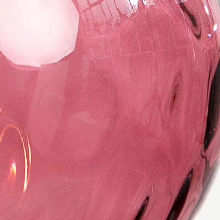 Gros plan sur la surface martelée d'un globe en verre soufflé aux reflets rosés