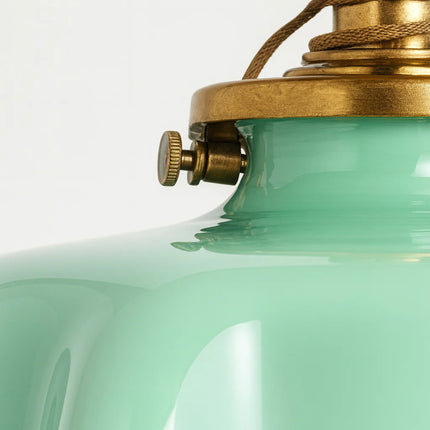 Zoom sur le bord ondulé de l'abat-jour en verre vert opalin et sa collerette en laiton doré