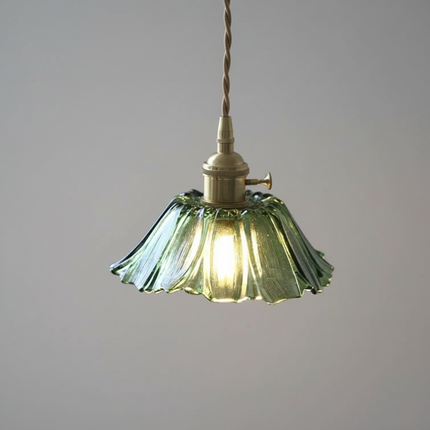 Suspension rétro en verre vert ondulé et laiton doré allumée sur fond gris, halo chaud