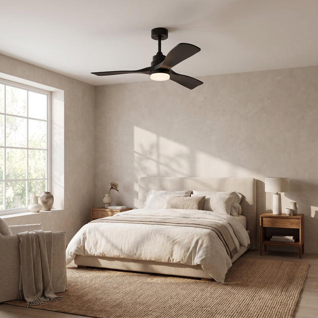 Ventilateur de plafond noir mat dans une chambre beige lumineuse, vu depuis le pied du lit