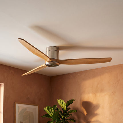 Trois pales en bois clair d'un ventilateur de plafond bas, mur terracotta et lumière chaude