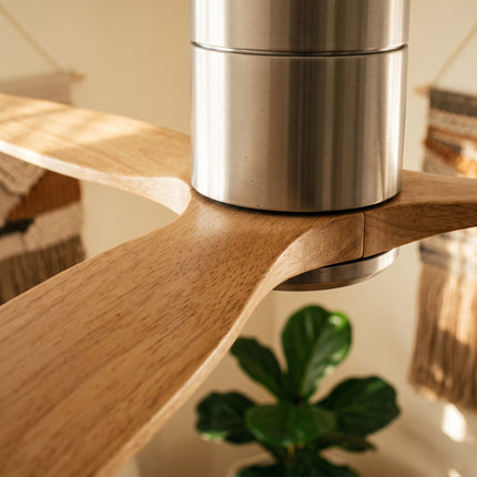 Gros plan sur une pale en bois clair et le moyeu argent brossé du ventilateur de plafond