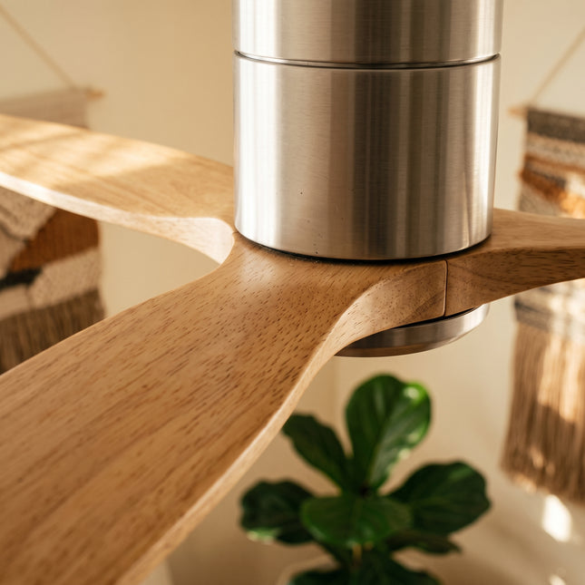 Gros plan sur une pale en bois clair et le moyeu argent brossé du ventilateur de plafond