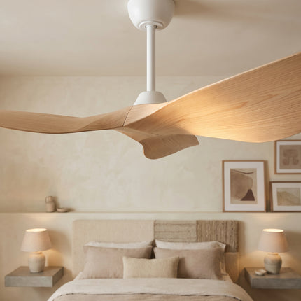 Vue rapprochée du ventilateur de plafond blanc et de ses trois pales incurvées effet bois clair, dans une chambre