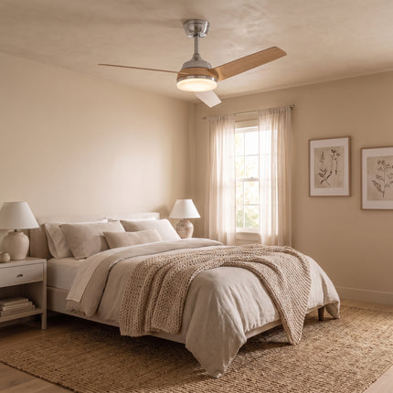 Ventilateur de plafond bois clair allumé dans une chambre beige, au-dessus d'un lit en lin et plaid tricoté