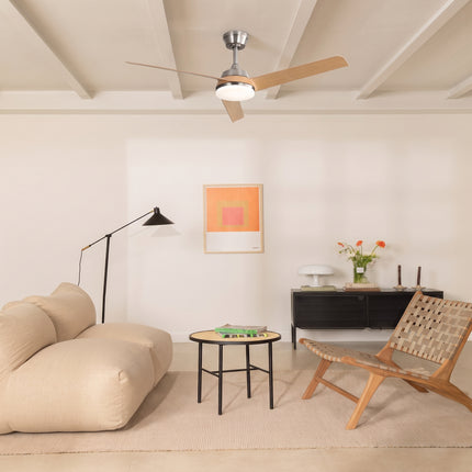 Ventilateur de plafond bois clair et nickel installé sur un plafond à poutres dans un salon beige lumineux